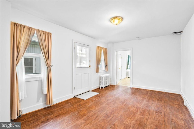 interior space featuring baseboards, wood finished floors, visible vents, and radiator