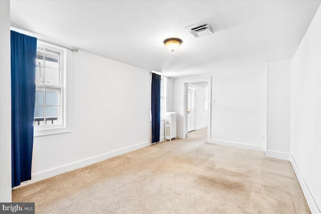 carpeted empty room featuring radiator heating unit, visible vents, and baseboards