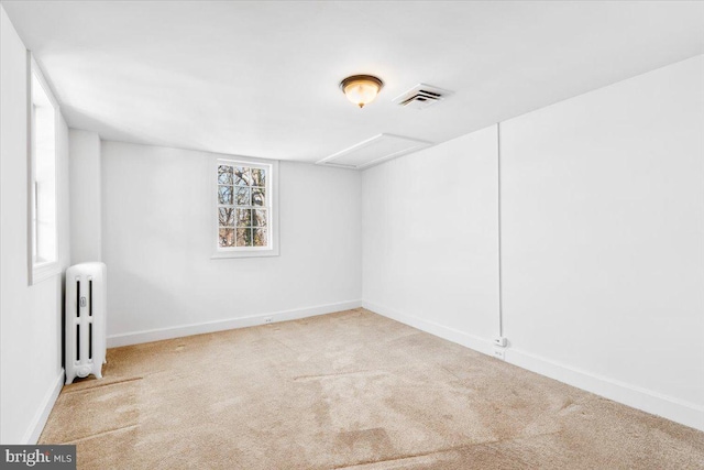 empty room with attic access, visible vents, baseboards, radiator, and carpet floors