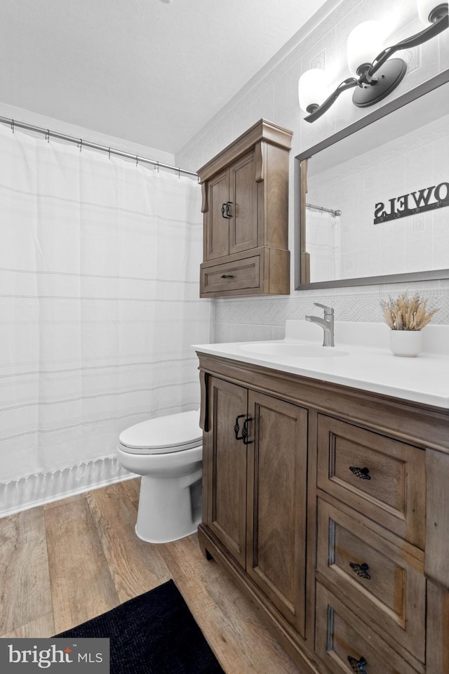 bathroom with toilet, vanity, tile walls, and wood finished floors