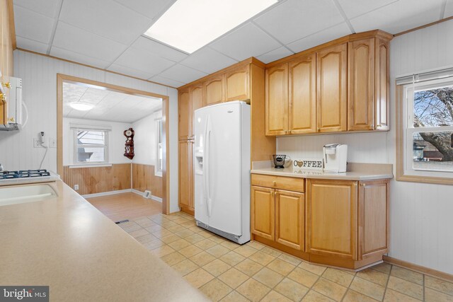 kitchen with a paneled ceiling, white fridge with ice dispenser, wooden walls, and light countertops