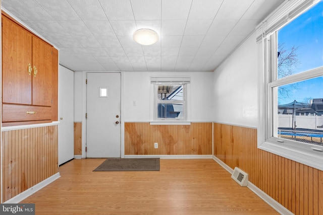 foyer with a wealth of natural light, visible vents, wainscoting, and light wood-type flooring