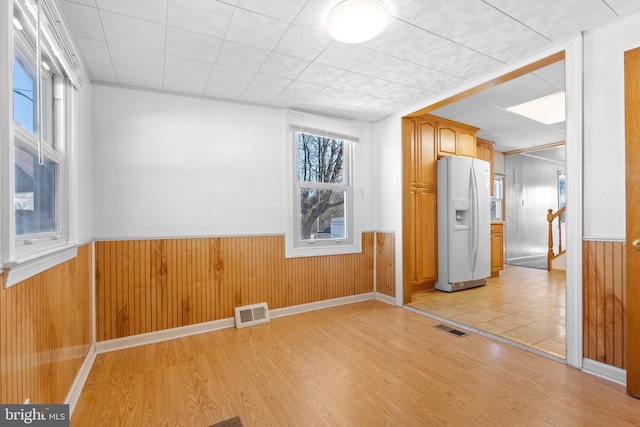 empty room with light wood-style floors, visible vents, wooden walls, and a wainscoted wall