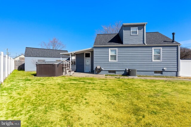 rear view of house with central AC unit, a lawn, a fenced backyard, and a shingled roof