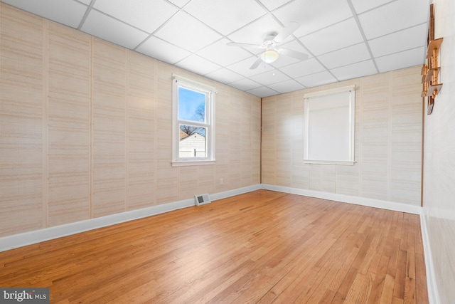 unfurnished room featuring visible vents, a ceiling fan, a drop ceiling, light wood-style floors, and baseboards