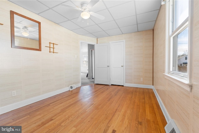 empty room featuring hardwood / wood-style floors, visible vents, a drop ceiling, and ceiling fan