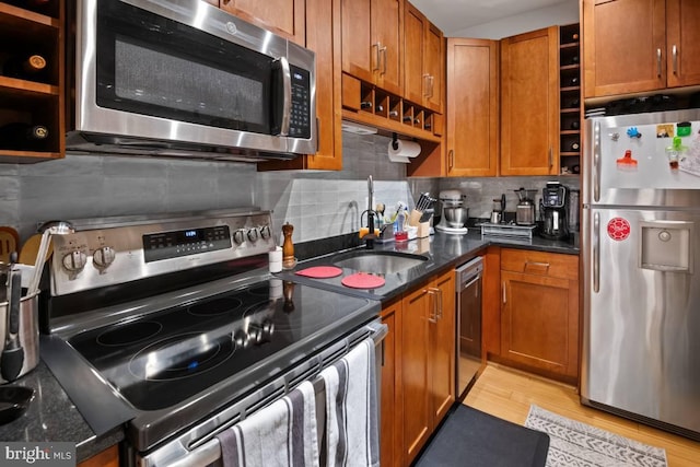 kitchen with brown cabinets, open shelves, appliances with stainless steel finishes, light wood-style floors, and a sink