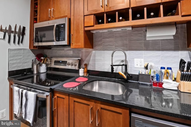 kitchen with dark stone counters, appliances with stainless steel finishes, a sink, and brown cabinets