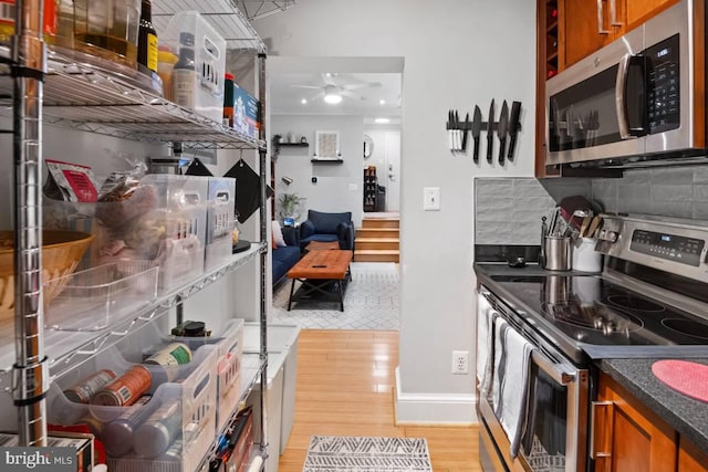 kitchen featuring appliances with stainless steel finishes, backsplash, brown cabinets, light wood finished floors, and dark countertops