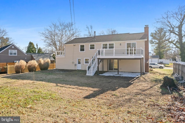 rear view of house featuring a chimney, stairway, fence, a deck, and a yard