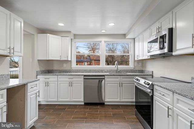 kitchen featuring white cabinets, light stone counters, stainless steel appliances, and wood finish floors