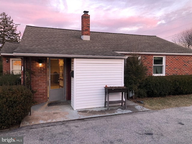 rear view of house featuring a shingled roof, a chimney, and brick siding