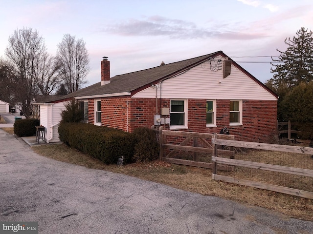 view of front facade with brick siding, a chimney, and fence