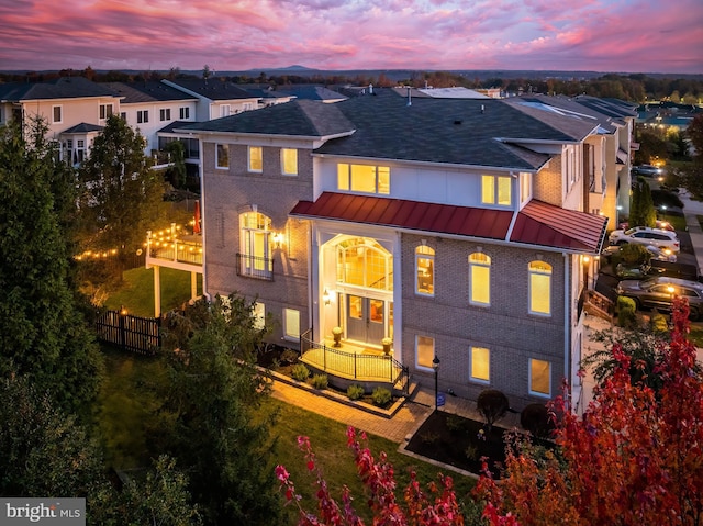 view of front facade with metal roof, brick siding, fence, a residential view, and a standing seam roof