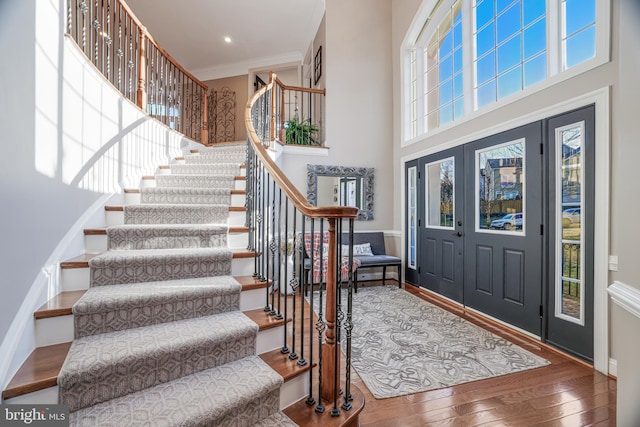 entryway featuring ornamental molding, stairway, a towering ceiling, and wood finished floors