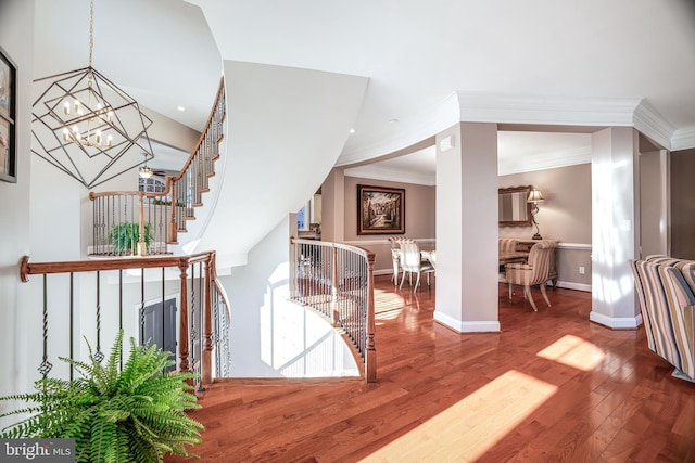 hall with baseboards, wood finished floors, crown molding, an upstairs landing, and a chandelier