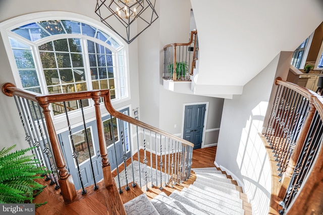 staircase featuring an inviting chandelier, a high ceiling, baseboards, and wood finished floors