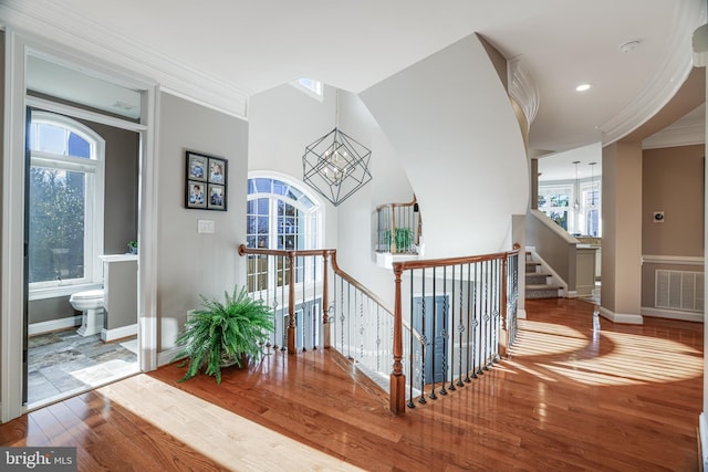 hall featuring wood finished floors, visible vents, baseboards, an inviting chandelier, and crown molding