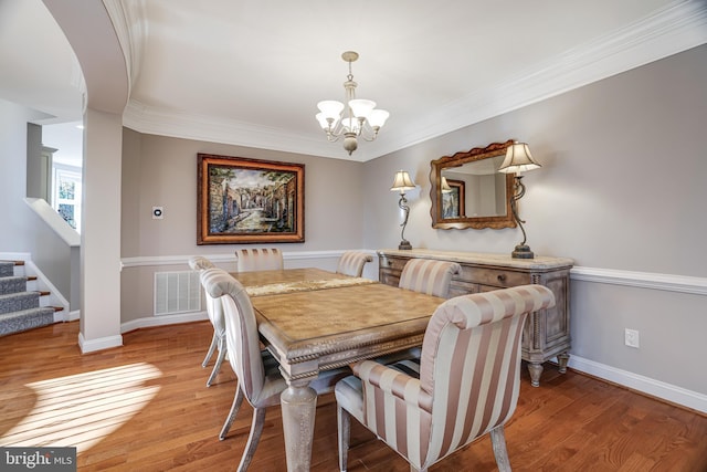 dining space featuring light wood finished floors, visible vents, an inviting chandelier, ornamental molding, and stairs