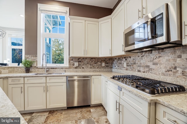 kitchen featuring appliances with stainless steel finishes, backsplash, a sink, and light stone countertops