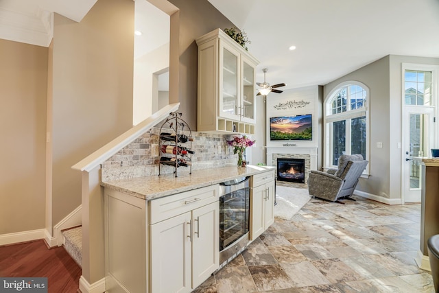 kitchen featuring beverage cooler, backsplash, light stone countertops, a glass covered fireplace, and glass insert cabinets