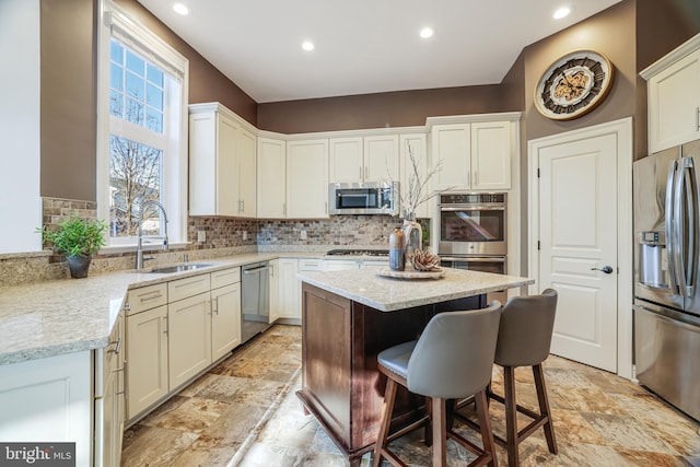 kitchen with tasteful backsplash, a kitchen island, light stone counters, stainless steel appliances, and a sink