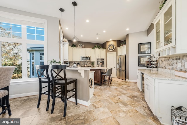 kitchen with light stone counters, decorative light fixtures, a breakfast bar area, appliances with stainless steel finishes, and glass insert cabinets