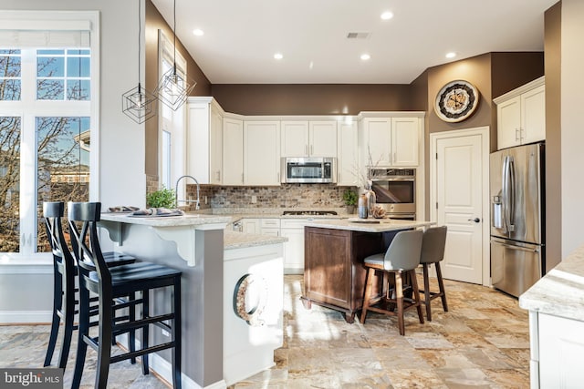 kitchen with visible vents, a kitchen island, a breakfast bar, stainless steel appliances, and backsplash