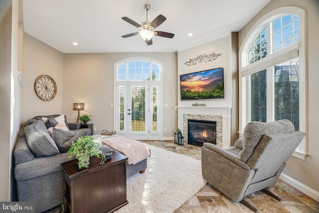 living area with ceiling fan, stone finish floor, a glass covered fireplace, and baseboards