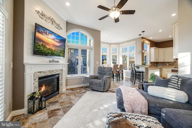 living room with a fireplace, recessed lighting, stone tile flooring, a ceiling fan, and baseboards