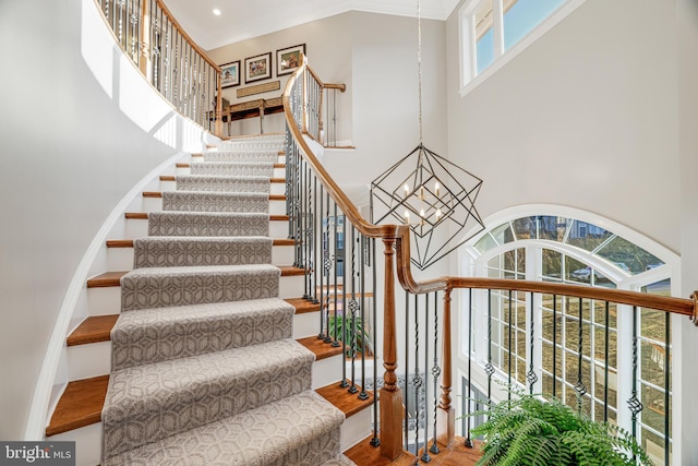 stairs with a towering ceiling, a chandelier, crown molding, and wood finished floors