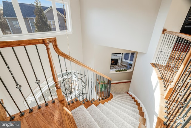 stairway featuring a warm lit fireplace, wood finished floors, and baseboards