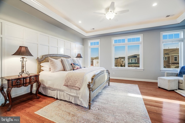 bedroom with recessed lighting, wood finished floors, baseboards, a tray ceiling, and crown molding