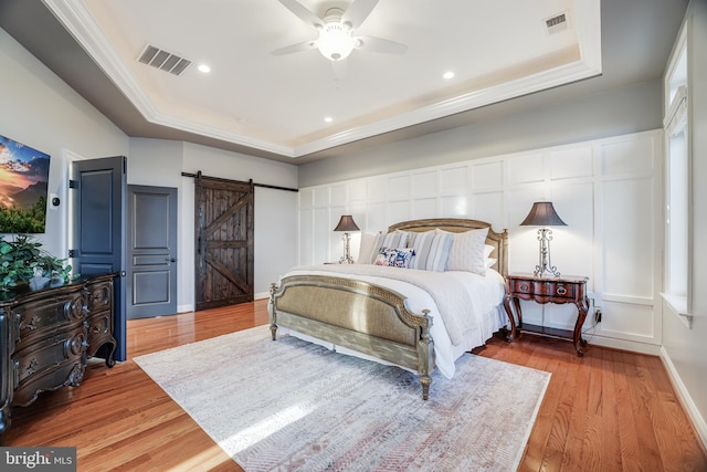 bedroom with a raised ceiling, visible vents, a barn door, ornamental molding, and wood finished floors