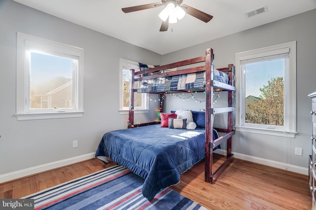 bedroom featuring baseboards, multiple windows, visible vents, and wood finished floors