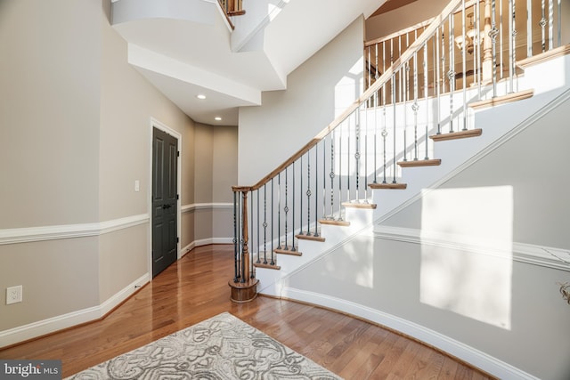 stairway with recessed lighting, a high ceiling, baseboards, and wood finished floors