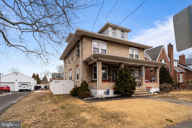 american foursquare style home with brick siding, a detached garage, an outbuilding, covered porch, and a front yard