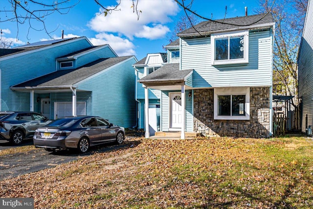 view of front of property featuring an attached garage, stone siding, driveway, roof with shingles, and a front yard