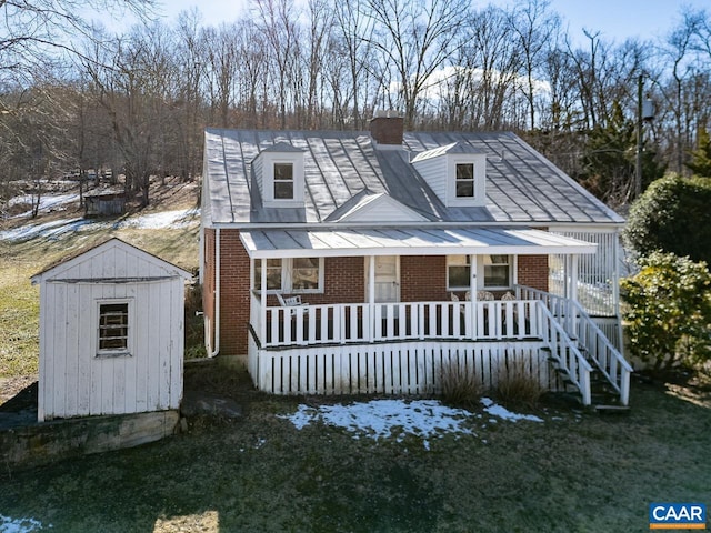 view of front of property featuring an outbuilding, a porch, brick siding, a storage unit, and a chimney