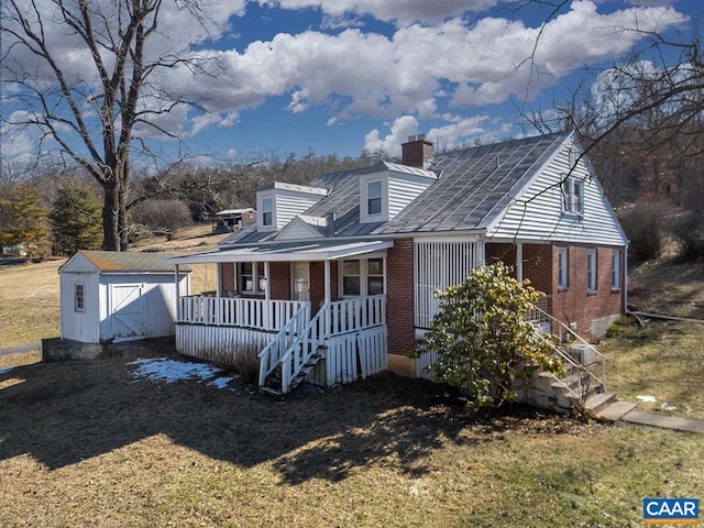 view of front of property with brick siding, a chimney, a porch, a storage shed, and an outdoor structure