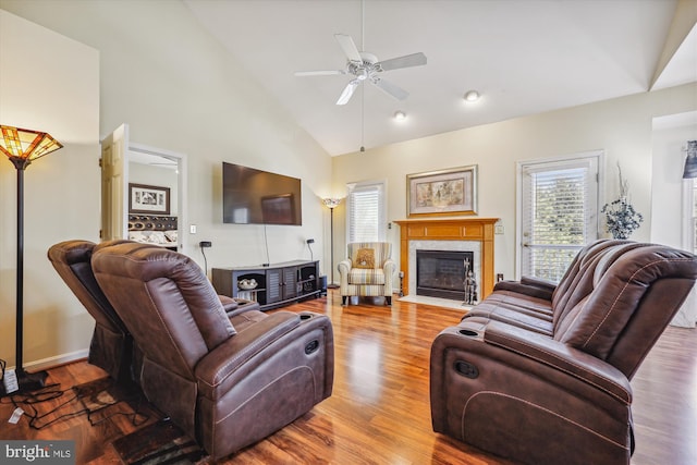 living room with baseboards, a ceiling fan, a fireplace with flush hearth, wood finished floors, and high vaulted ceiling