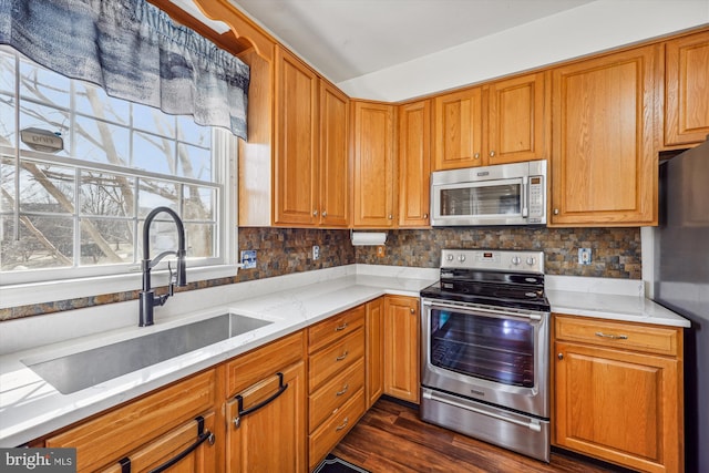 kitchen featuring dark wood-style flooring, a sink, light stone countertops, stainless steel appliances, and backsplash