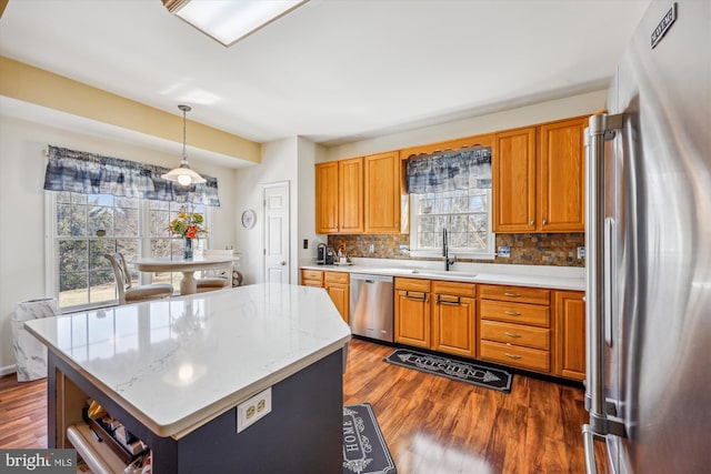 kitchen with stainless steel appliances, dark wood-style flooring, a sink, backsplash, and brown cabinetry