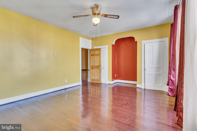 spare room with arched walkways, wood finished floors, a ceiling fan, and baseboards