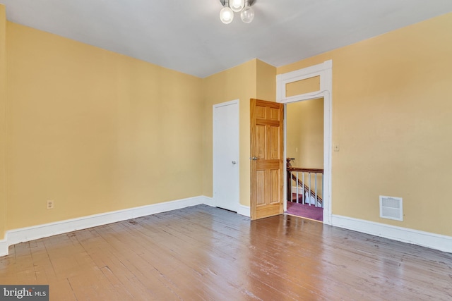 empty room featuring wood finished floors, visible vents, and baseboards