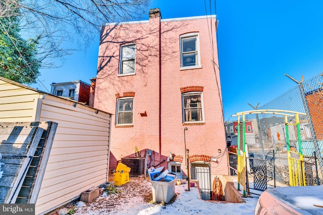 snow covered property with fence, cooling unit, and brick siding