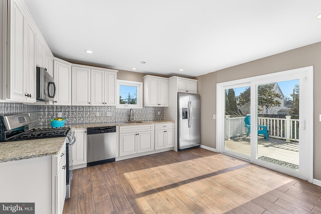 kitchen with appliances with stainless steel finishes, light wood-style floors, a sink, and decorative backsplash