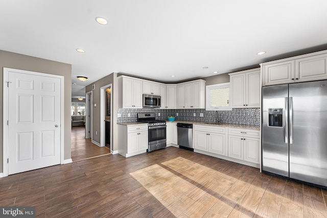 kitchen with dark wood finished floors, decorative backsplash, appliances with stainless steel finishes, white cabinetry, and a sink