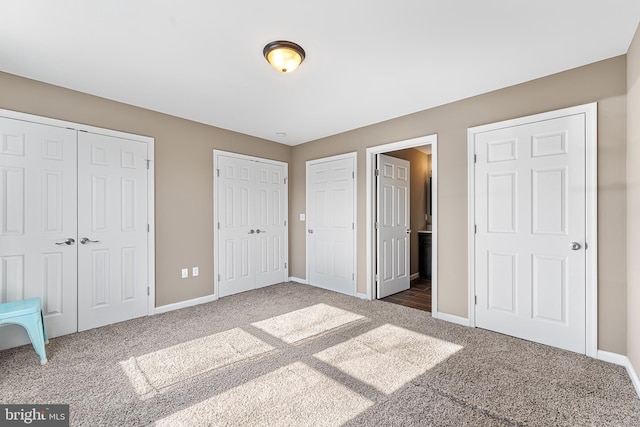 unfurnished bedroom featuring multiple closets, carpet flooring, and baseboards