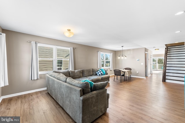 living area featuring light wood-style flooring, stairs, baseboards, and a chandelier